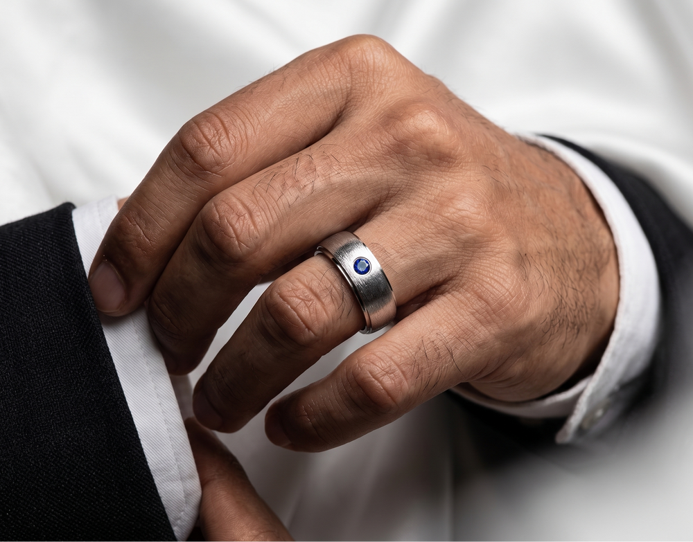 Hand wearing a silver ring with a blue gemstone, against a white background
