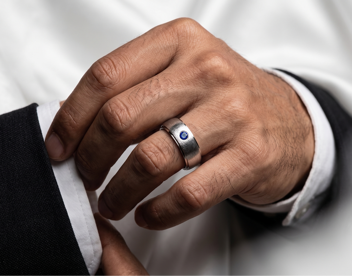 Hand wearing a silver ring with a blue gemstone, against a white background
