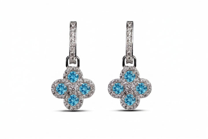A pair of silver-tone drop earrings featuring a four-petal flower design with bright blue center stones surrounded by small clear stones, shown on a plain white background.