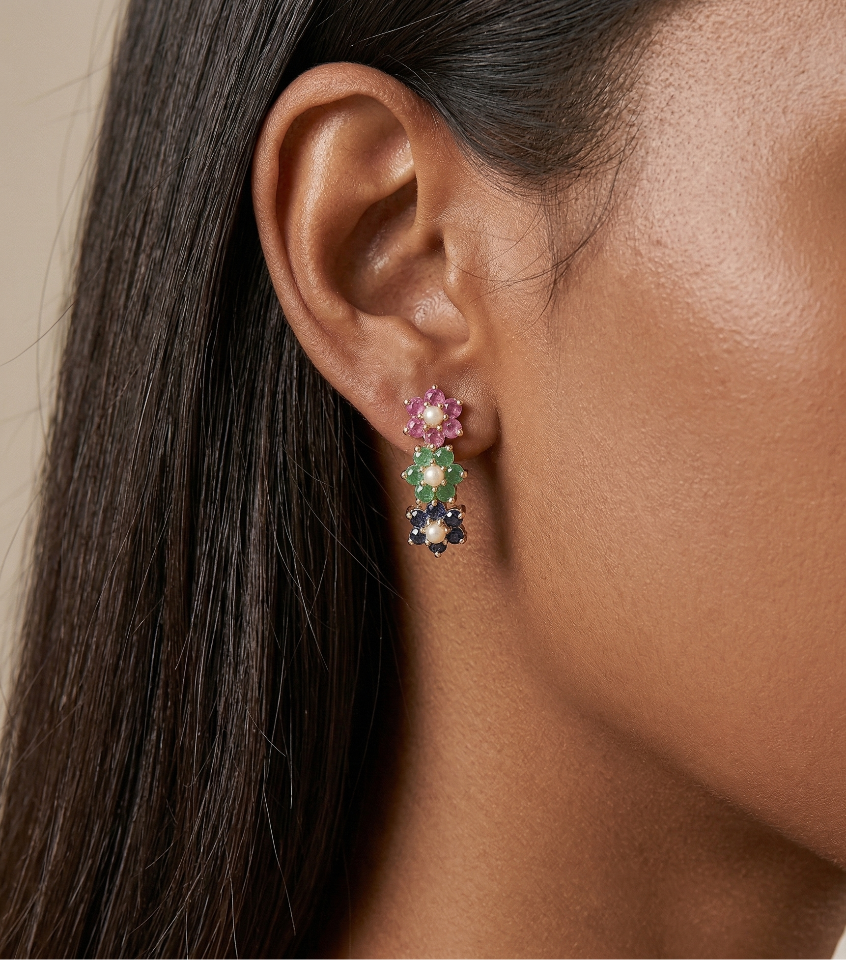 Close-up of a woman wearing colorful ruby, emerald and sapphire gemstone earrings with a neutral background