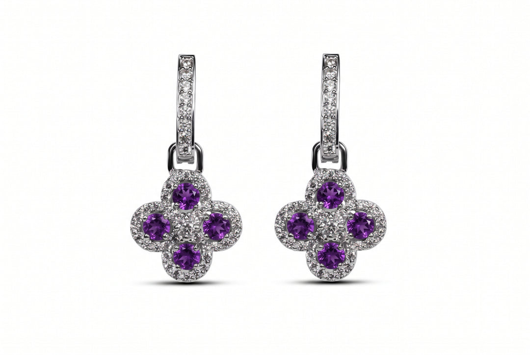 Pair of white gold drop earrings featuring a clover-shaped pendant set with four round purple amethyst gemstones and pavé-set diamonds, hanging from diamond-encrusted huggie hoops against a plain background.