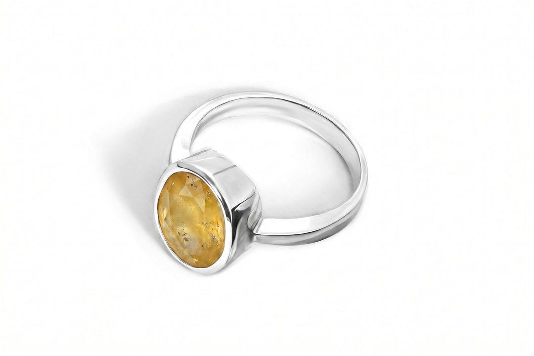 A silver ring featuring a bezel-set oval yellow sapphire gemstone, shown on a clean white background with a soft shadow.